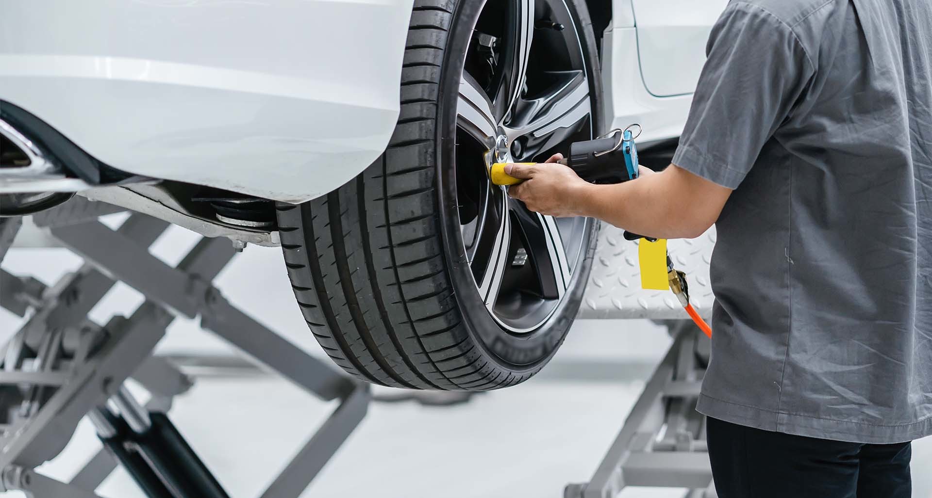 Mechaniker bearbeitet einen Autoreifen an einem auf einer Hebebühne angehobenen Fahrzeug – typische Anwendung von Werkstattausrüstung für sichere Hubtechnik in Werkstätten.