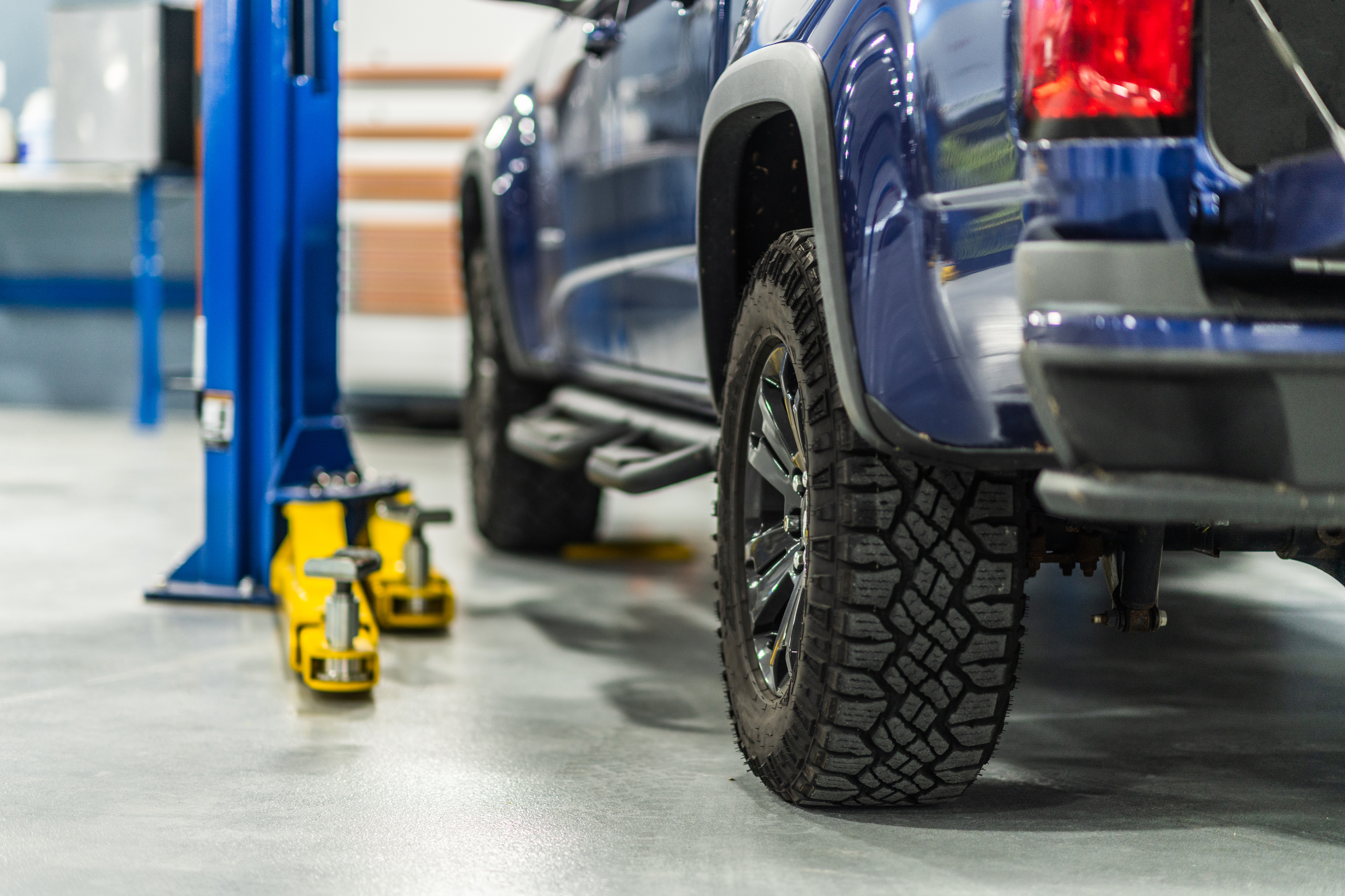 Blauer Pick-up auf einer blauen Hebebühne in einer Werkstatt, begleitet von gelben Bodenhebern – zeigt die sichere und zuverlässige Hubtechnik, die AH Werkstatt Service für Werkstätten und gewerbliche Betreiber anbietet.