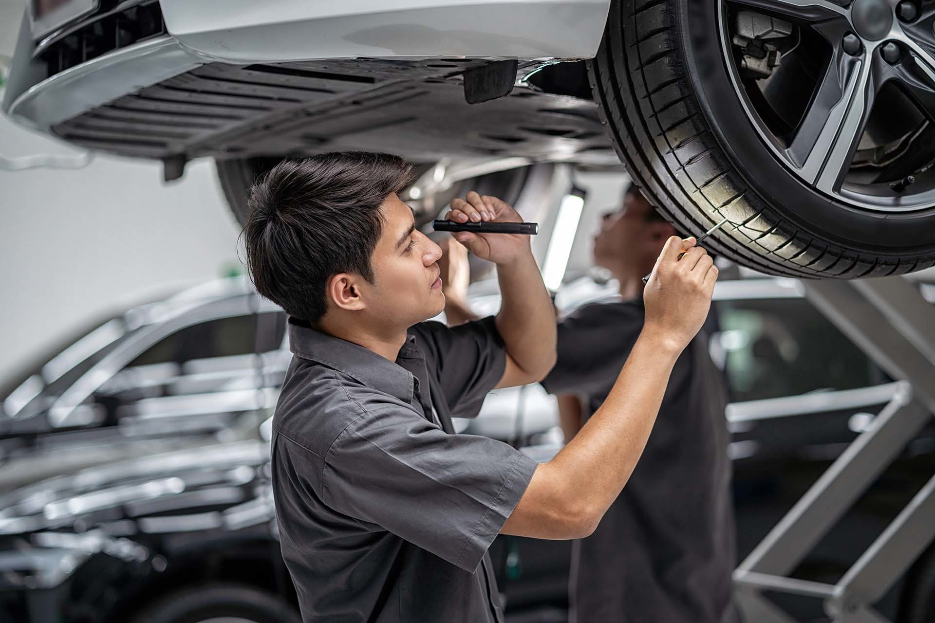 Zwei Mechaniker prüfen ein Auto unter einer Hebebühne in einer Werkstatt, was die spezialisierten Dienstleistungen von AH Werkstatt Service für Werkstattausrüstung und Hebebühnenunterstützung widerspiegelt.
