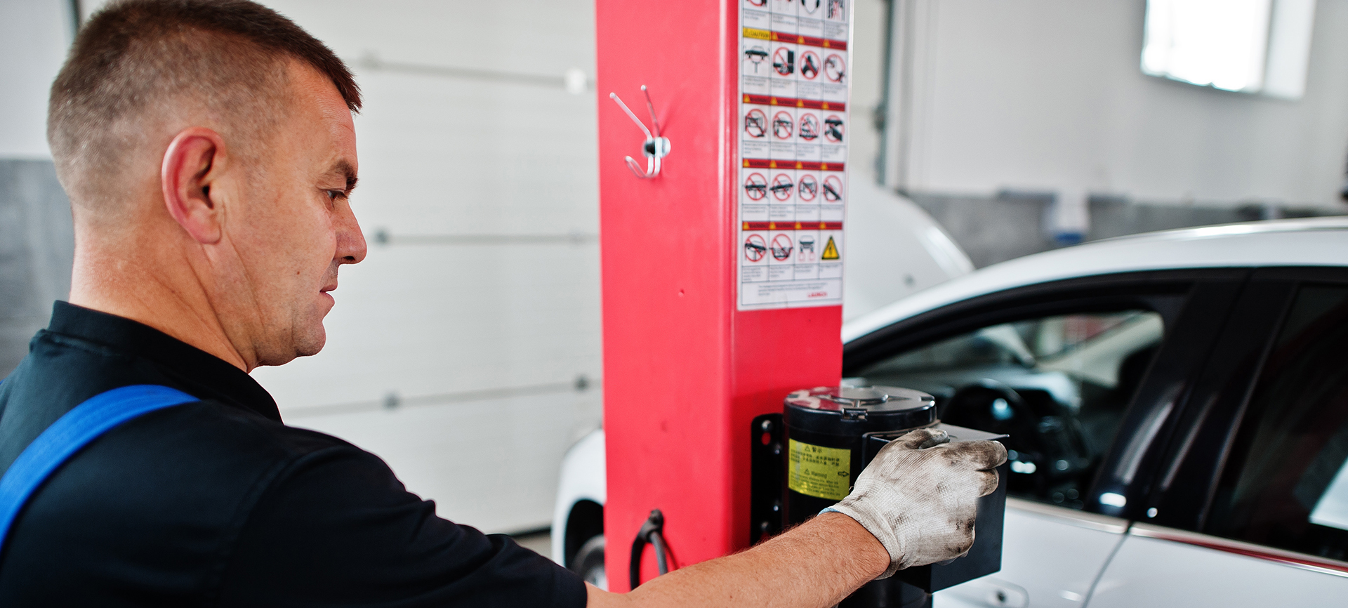 Mechaniker führt Wartungsarbeiten an einer Hebebühne in einer Werkstatt durch – AH Werkstatt Service spezialisiert auf Reparatur, Wartung und Sicherheitsprüfungen von Hebebühnen für zuverlässige Hubtechnik.