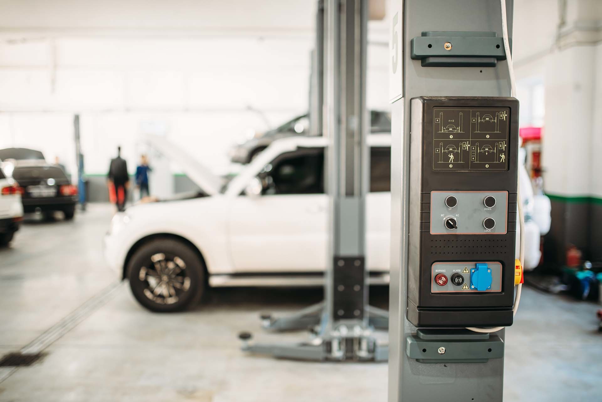Hebebühne mit Steuerung in einer Werkstatt, auf der ein weißes Fahrzeug positioniert ist – Beispiel für die Hubtechnik-Lösungen von AH Werkstatt Service.