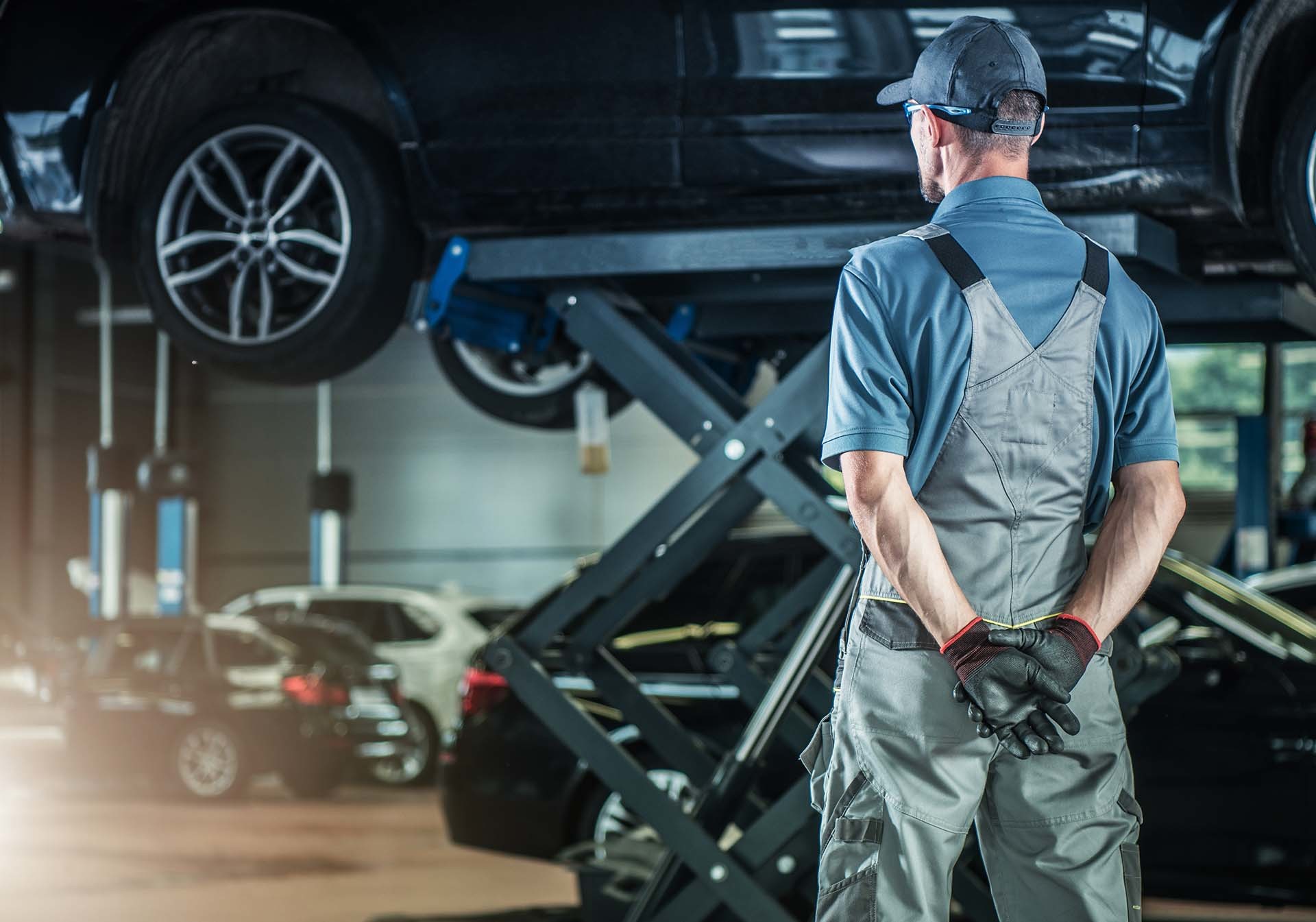 Ein Mechaniker beobachtet ein Auto auf einer Hebebühne in einer Werkstatt – ein Beispiel für die spezialisierten Dienstleistungen von AH Werkstatt Service im Bereich Hebetechnik und Werkstattausrüstung.